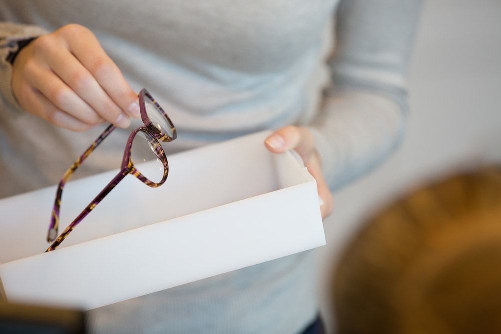 Eine Optikerin hält eine Brille in der Hand. Sie zeigt sie dem Kunden. Die Brille ist braun gemustert und wirkt sehr sportlich durch die Musterung.